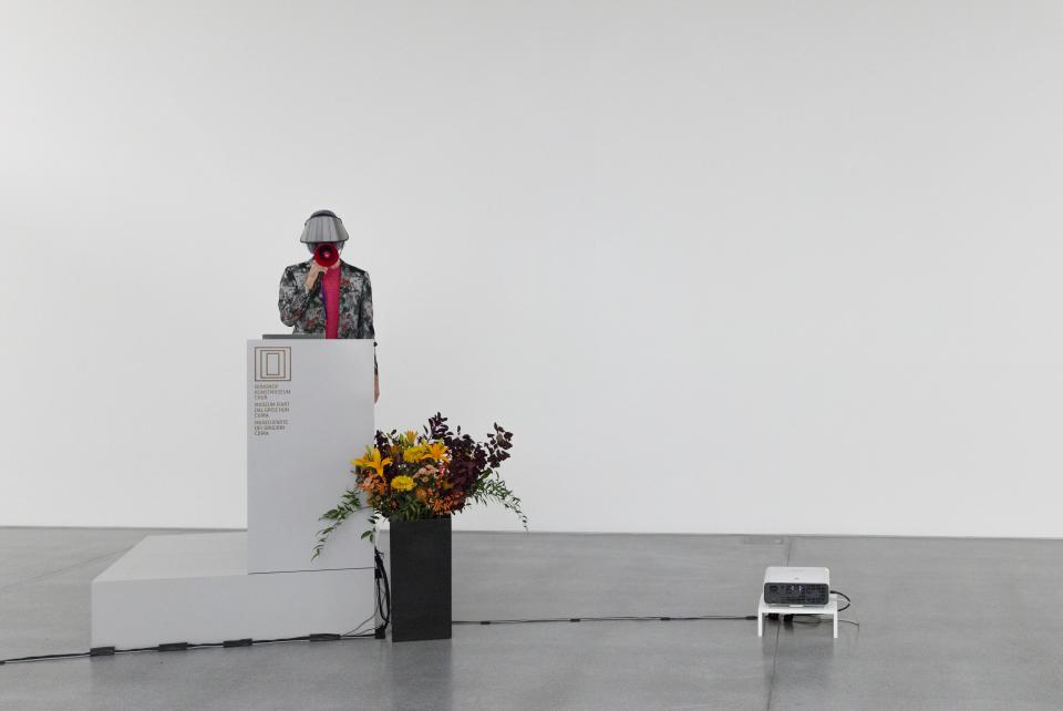 masked performer standing on podium with red megaphone