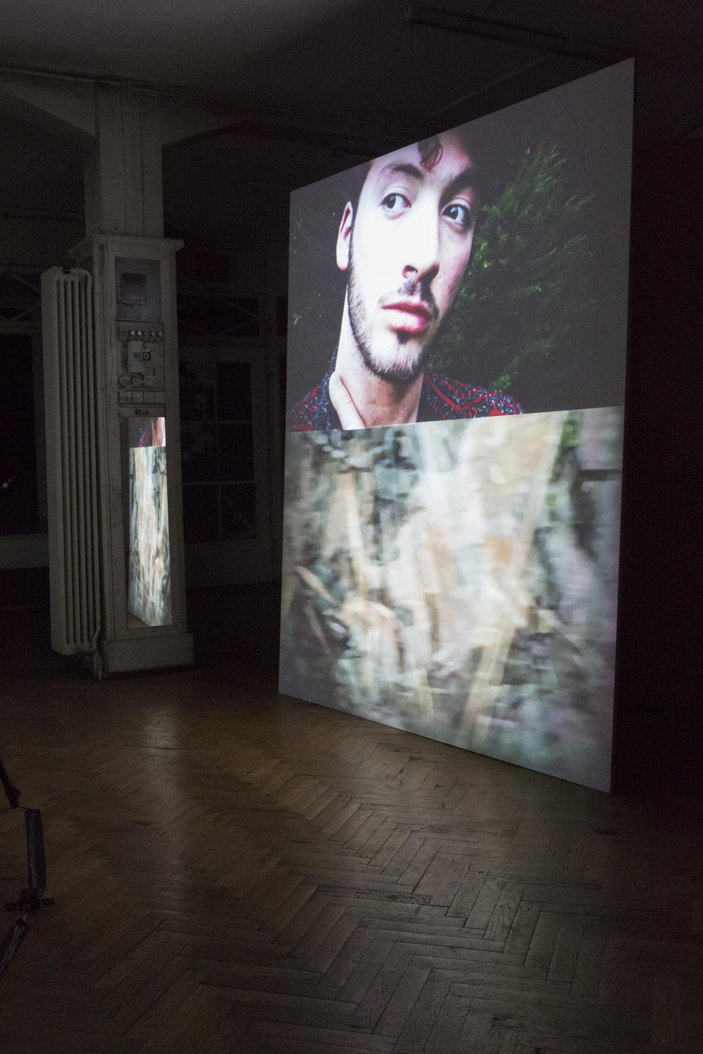 two projections (one of face of artist, one of abstract pattern) on top of each other on bog woodboard in room