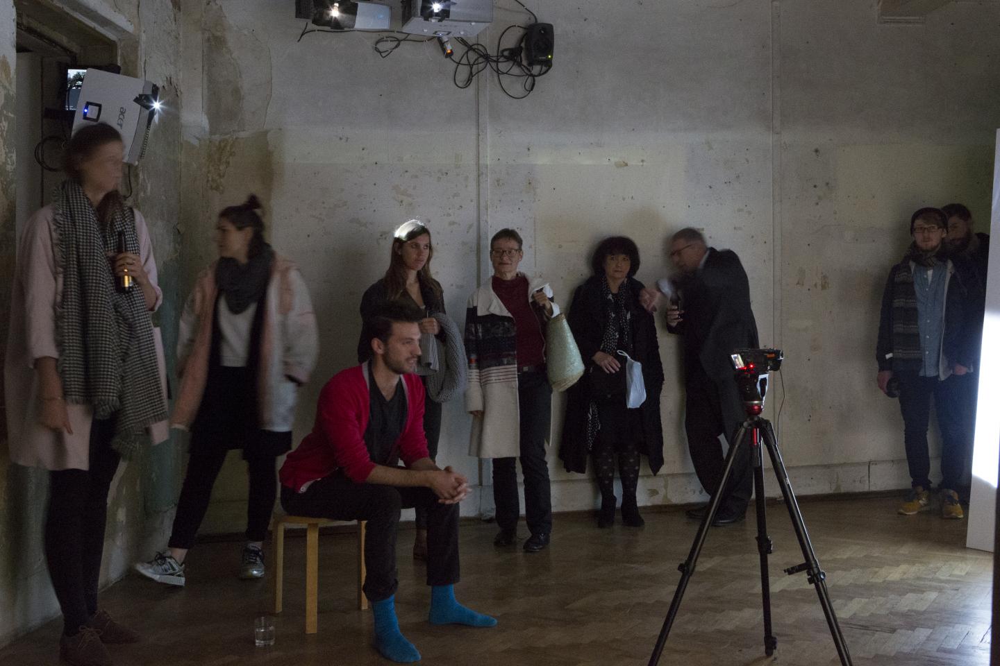 performer sitting in front of a video camera, surrounded by audience