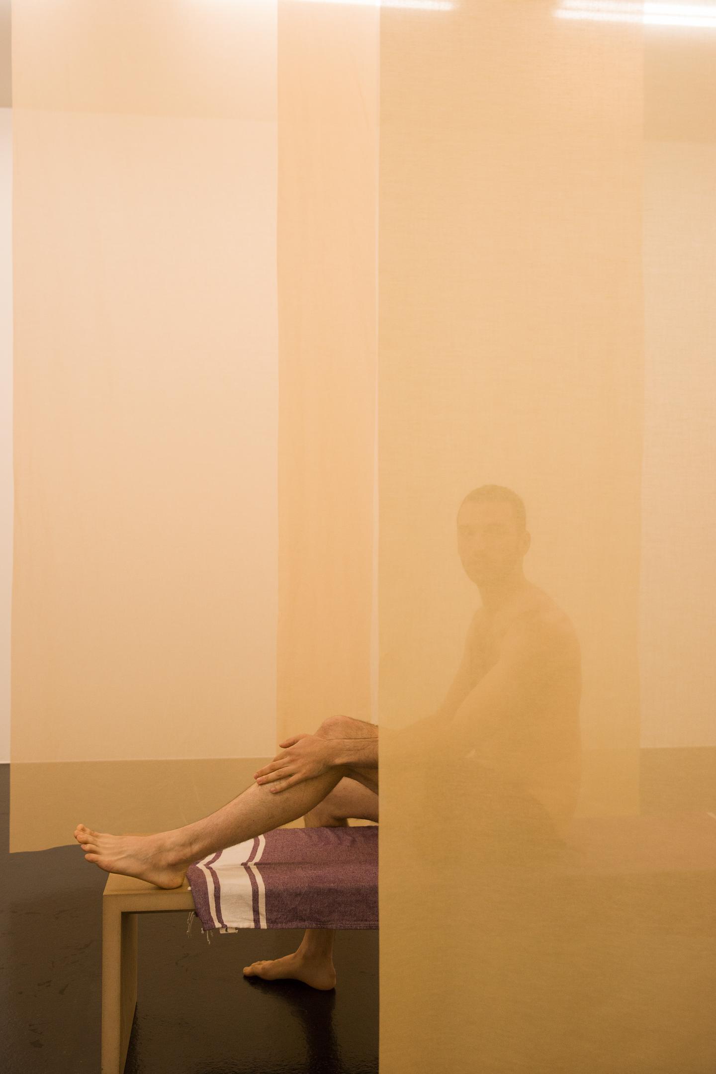 artist sitting on wooden bench behind transparent curtain